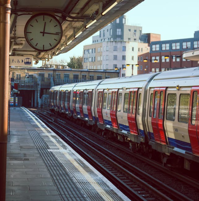 A London Underground train with a red and blue livery is stationary at Bermondsey station platform. The platform features tactile paving along the edge for safety, and overhead lighting illuminates th